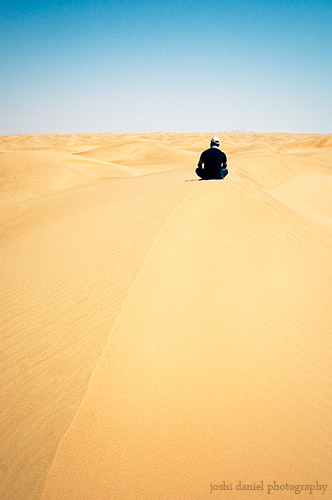 Photograph of Dinu Varghese sitting on a sand dune in United Arab Emirates